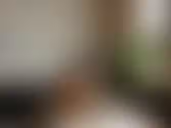 Expat man in a brown blazer eating takeout at a laptop in a cozy office with plants, art, and exposed brick. Bright window light. Urban vibe.